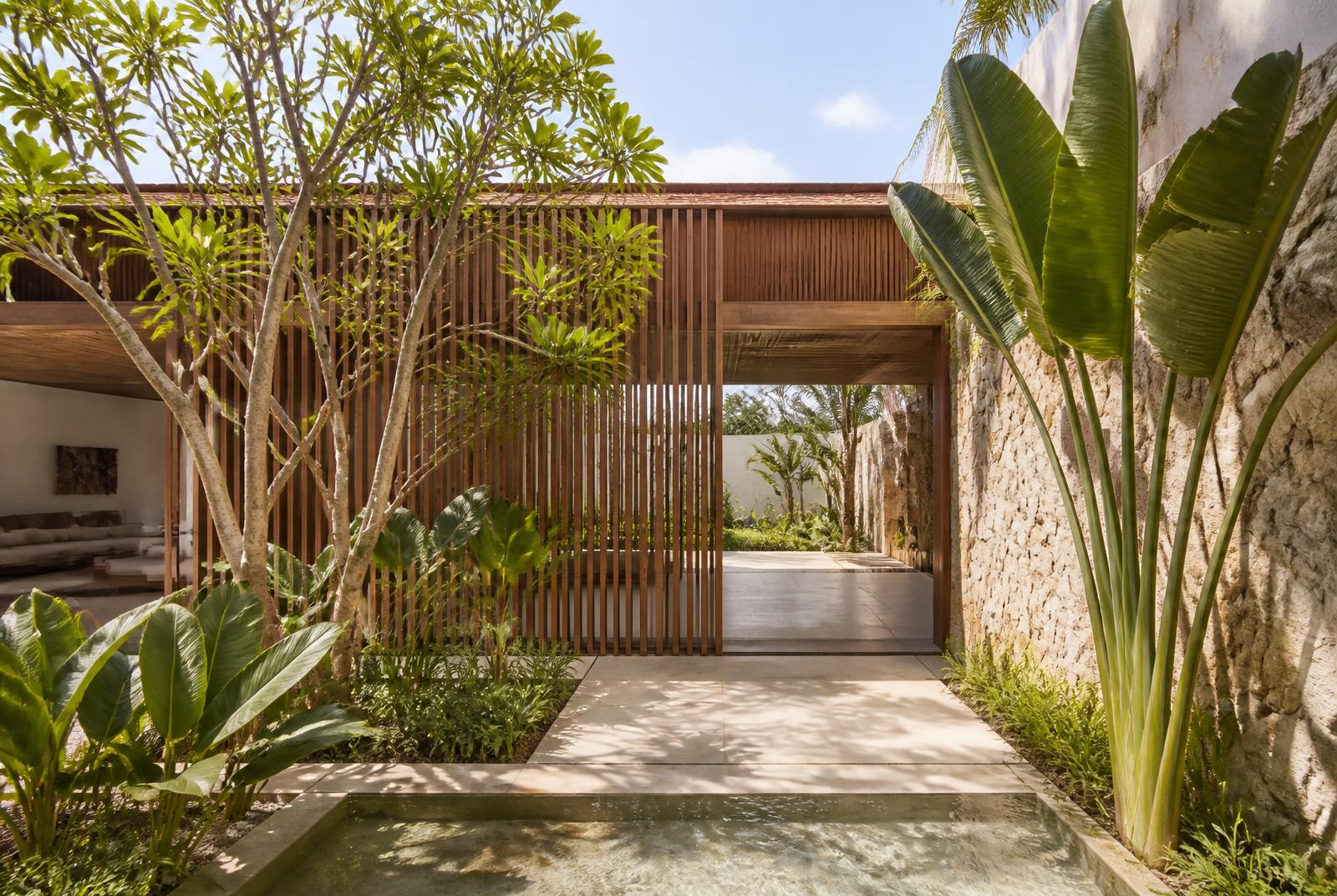 Jardim tropical integrado à arquitetura com pedra, madeira e água corrente