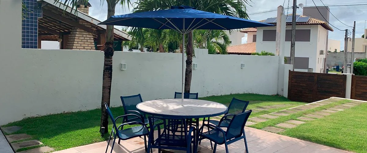 Ombrelone azul de haste central sobre mesa e cadeiras em um jardim.
