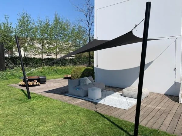Tenda tensionada escura sobre poltronas em deck junto a um jardim.