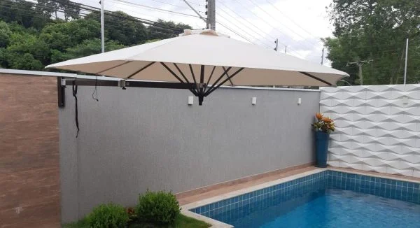 Ombrelone de parede com cobertura clara sobre uma piscina residencial.